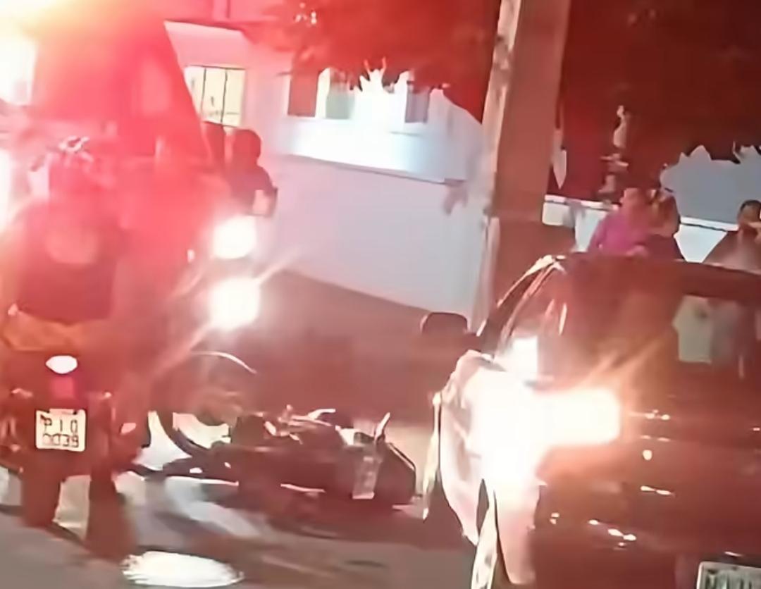 Na imagem é possível ver uma moto caída em via pública em frente à escola normal de Picos e vários veículos e outras motocicletas parados em frente ao local do acidente